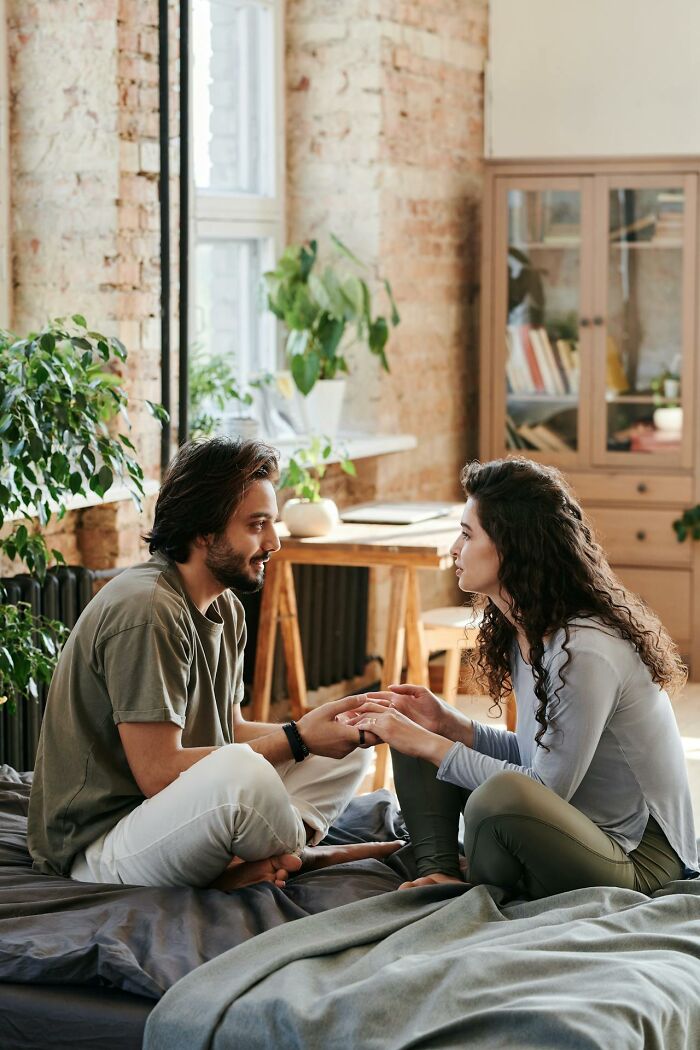 Couple sitting on bed holding hands and having a serious conversation about harsh truths of marriage reality.