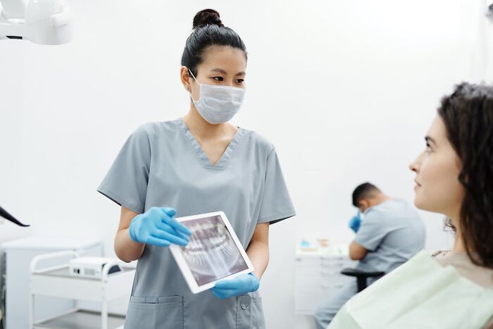 Dentist in scrubs and mask showing dental X-ray to patient during consultation in a modern dental clinic.