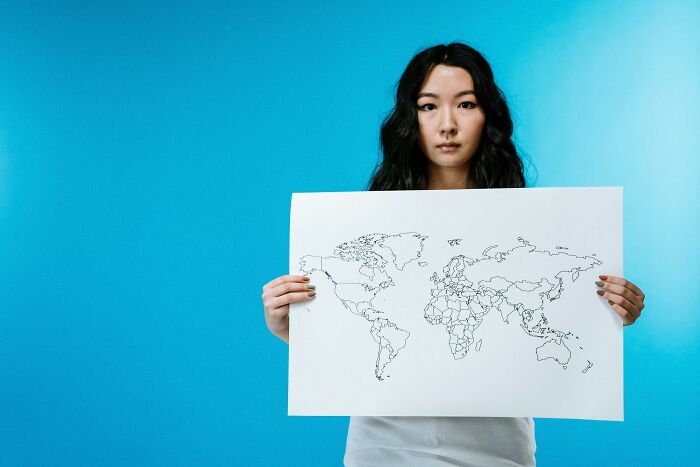 Young woman holding a blank world map illustration against blue background, visual geography challenges concept.
