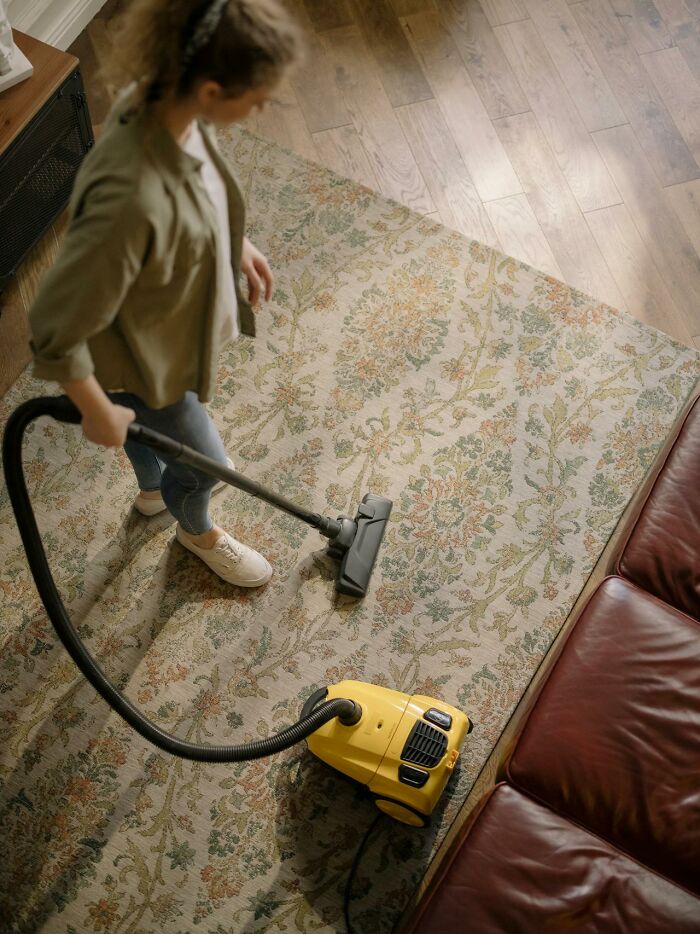 Woman vacuuming a floral rug in living room, illustrating childhood habits that were anything but normal realization.