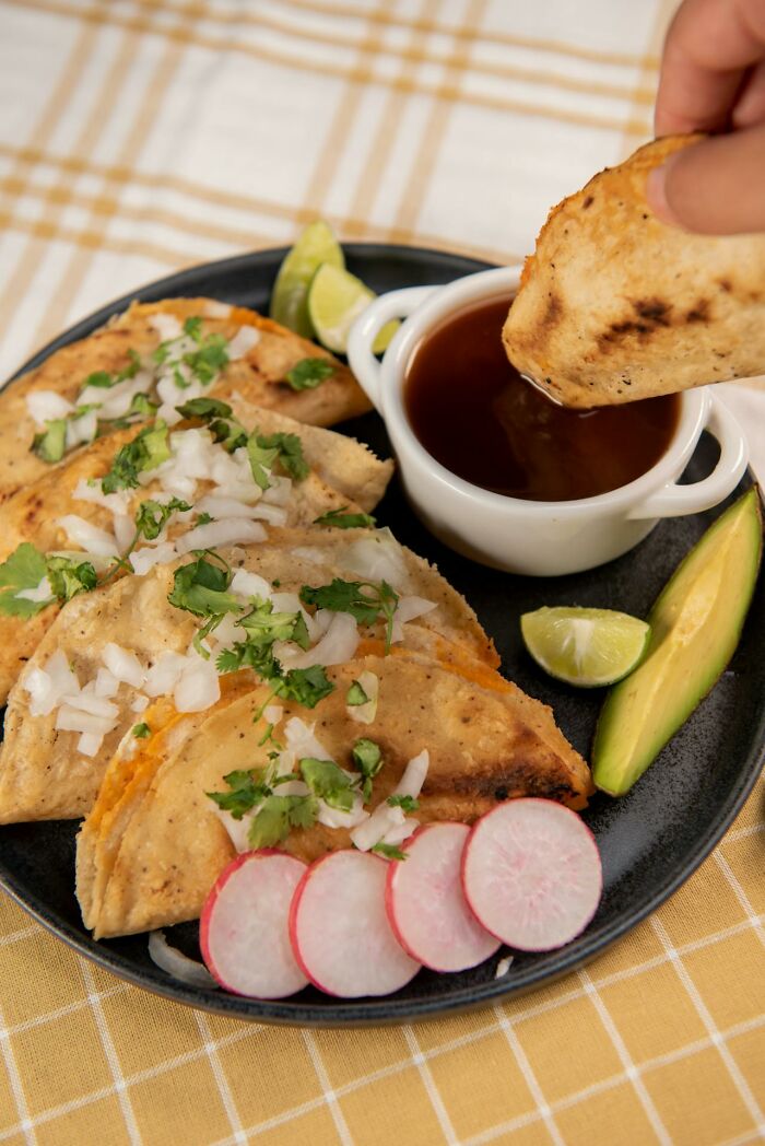 Plate of tacos with onions, cilantro, radishes, avocado, and a hand dipping a taco into sauce, illustrating examples of Karens.