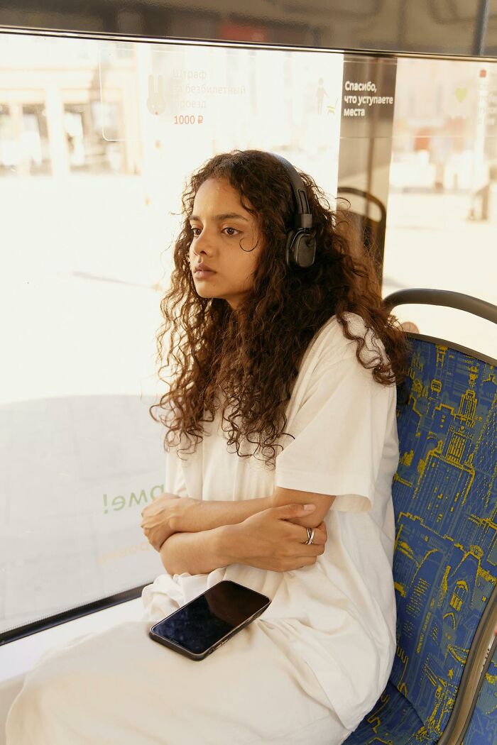 Young woman wearing headphones sitting quietly on public transport, embodying calmness amid chaotic Karen examples.