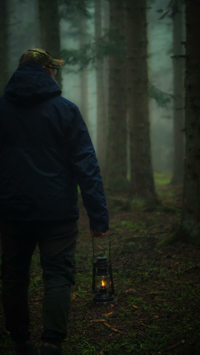 Park ranger holding a lantern walking through a foggy forest, capturing creepy and bizarre moments witnessed by hikers.