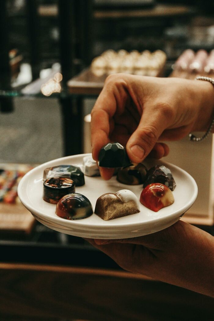 Hand holding a plate with assorted chocolates, demonstrating examples of Karens so crazy in a quirky setting.