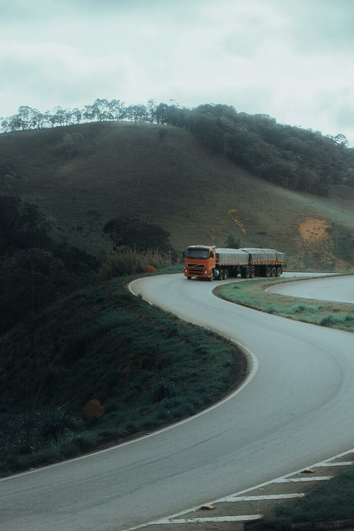 Orange semi-truck driving on a winding mountain road, illustrating haunting things truckers have seen on the road at night.
