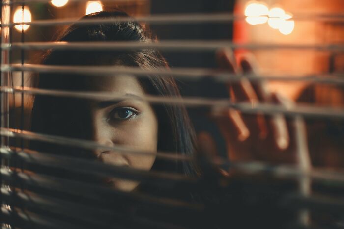 A woman looking through window blinds, conveying emotions linked to toxic relationship traits and emotional distress.