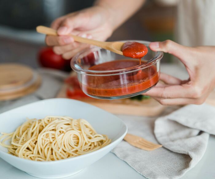 Hands holding a bowl of tomato sauce and spoon, preparing a meal, showing lovable clueless dads cooking while wives were pregnant.