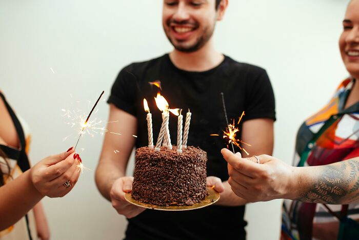 Group of people celebrating with a chocolate cake and sparklers, showing relatable and ridiculous moments together.
