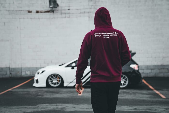 Person in a maroon hoodie walking near white and black cars in a parking lot, evoking real-life horror story vibes.