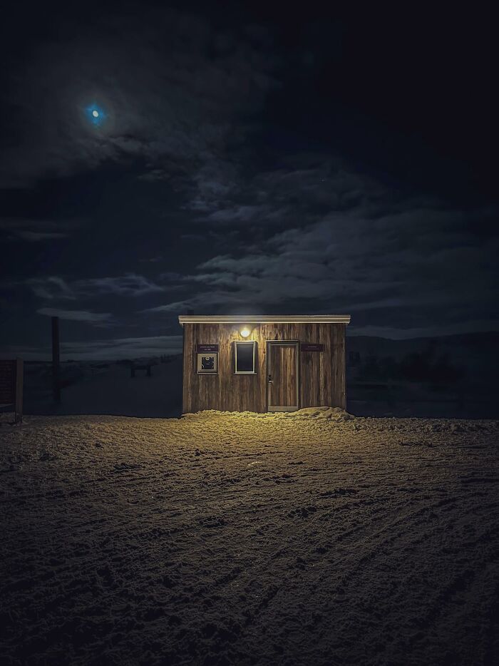 Small wooden cabin illuminated at night under a cloudy sky, evoking bizarre and creepy encounters by park rangers and hikers.