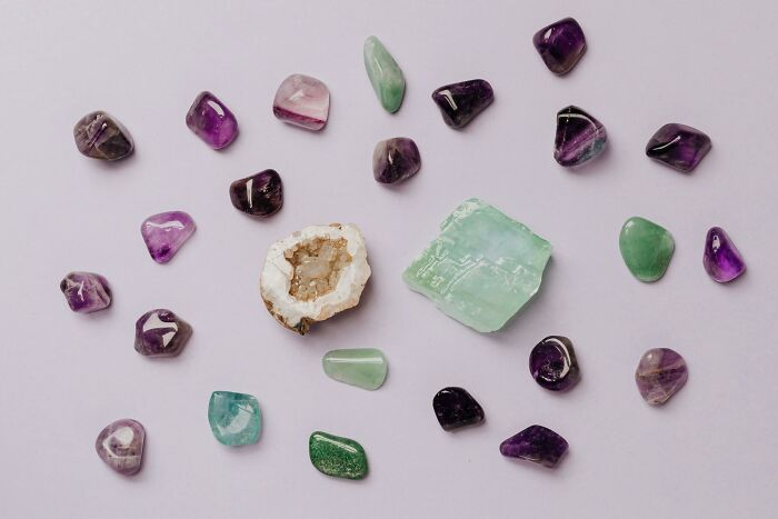 Assorted colorful polished gemstones and crystals arranged on a light purple background, unique and wild collection.