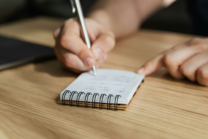 Person writing in a spiral notebook taking notes to prepare for SAT vocabulary questions for college acceptance. Person writing in a spiral notebook taking notes to prepare for SAT vocabulary questions for college acceptance.