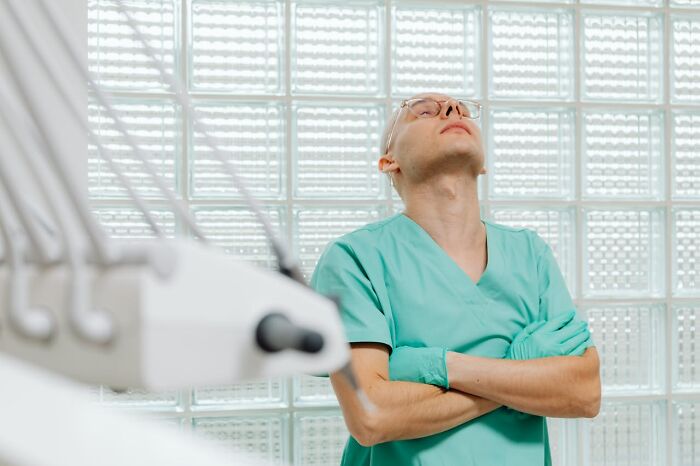 Man in green scrubs and glasses looking up thoughtfully in medical setting, capturing bizarre moments reflection.