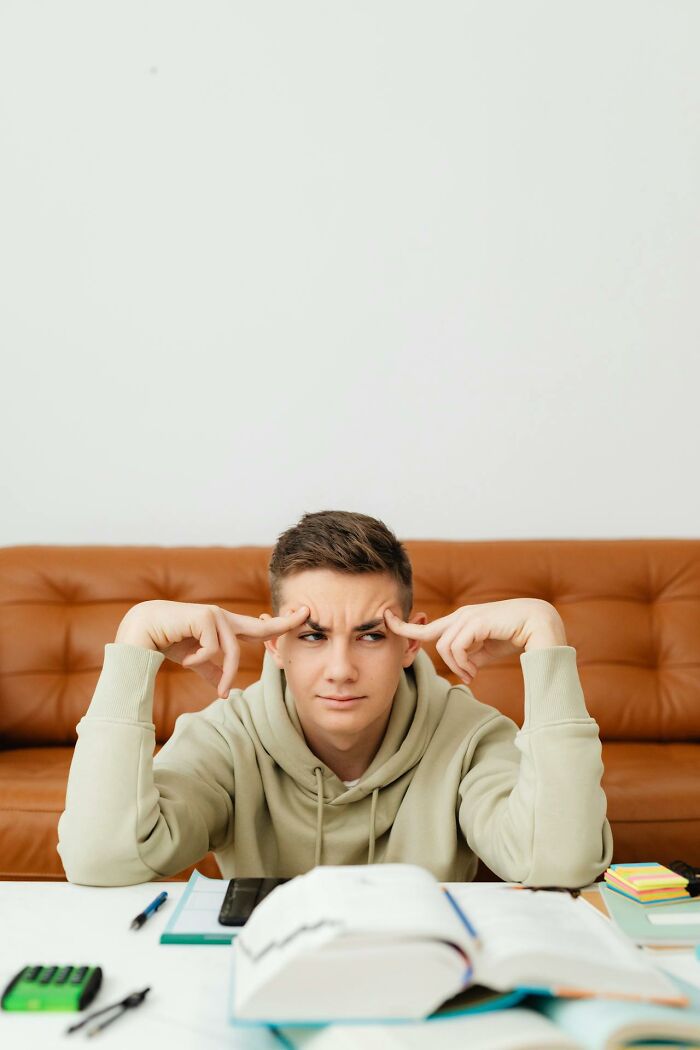 Young man looking puzzled while studying at a desk, capturing a bizarre moment making people wonder about sanity.