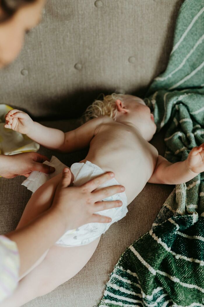 Adult changing diaper of a baby lying on a couch with a green striped blanket nearby in a home setting.