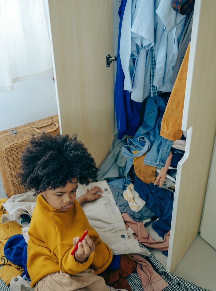 Child sitting amid messy clothes in a wardrobe, reflecting on unusual childhood habits and behaviors.