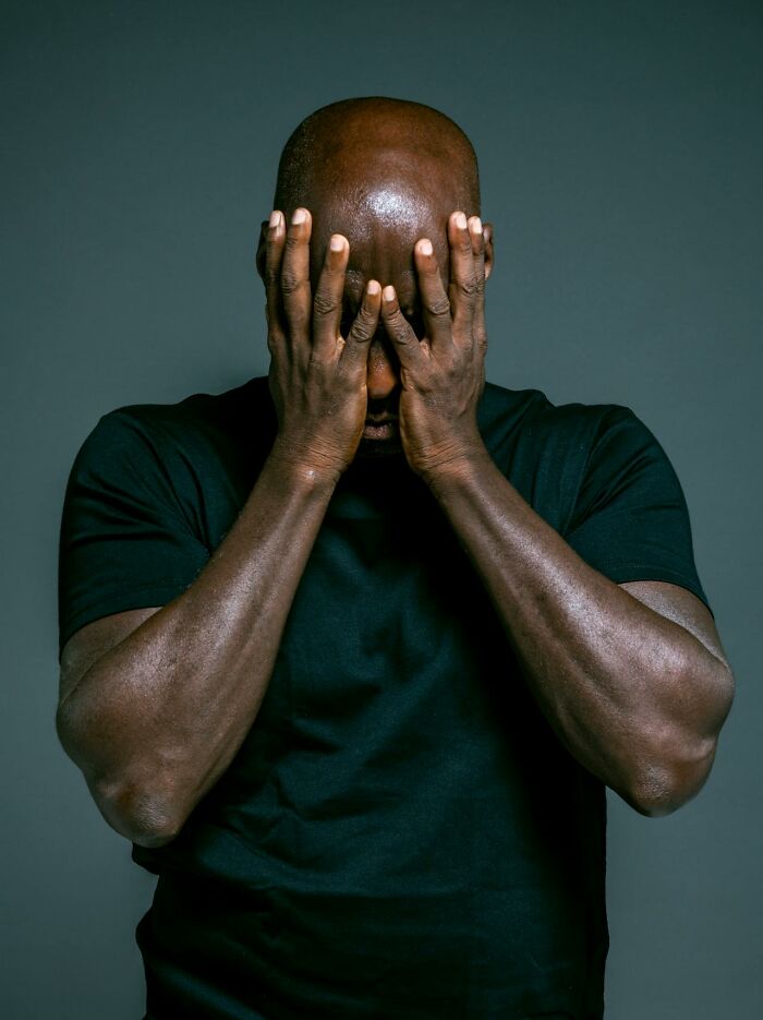 Man in black shirt covering his face with hands, expressing heavy emotions related to confessions and charges.