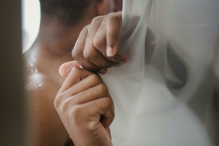 Person gripping a wet shower curtain, illustrating one of the ridiculous but relatable things many people do.
