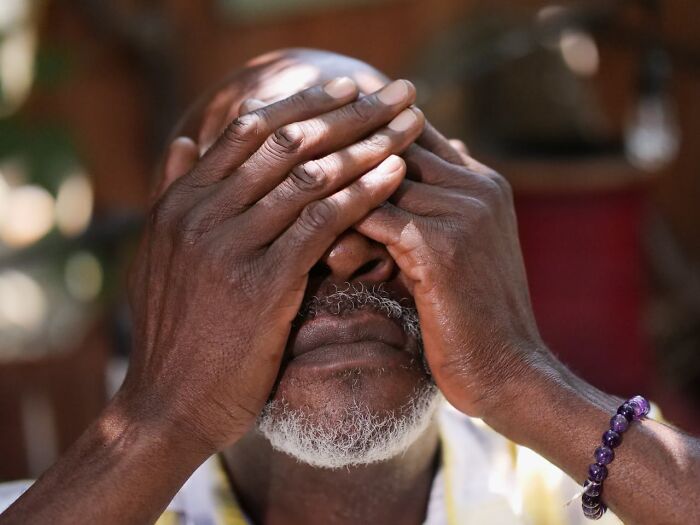 Elderly man covering his face with hands, expressing stress or haunting memories related to truckers on the road at night.