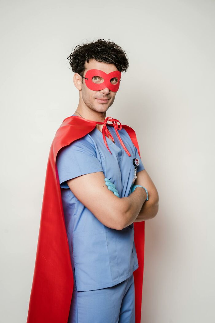 Man in scrubs wearing a red superhero cape and mask, posing confidently in a bizarre moment of playful sanity.