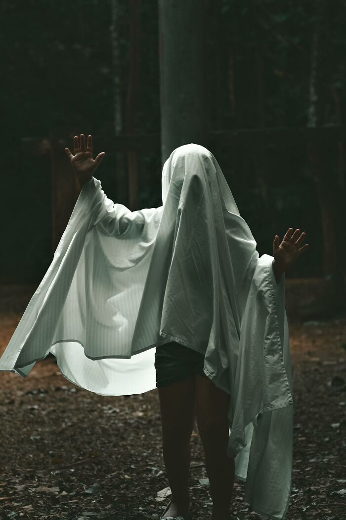 Person covered in a white sheet posing as a ghost in a dark forest, symbolizing haunting things truckers see at night.