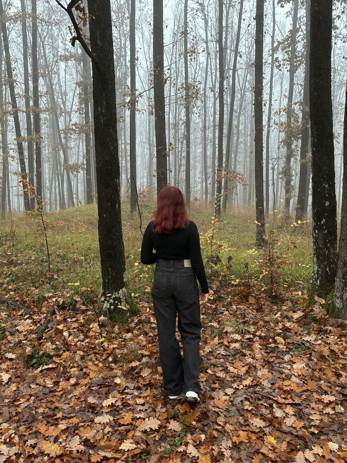 Woman with red hair walking alone in a foggy forest covered with leaves, evoking bizarre and creepy park ranger and hiker experiences.