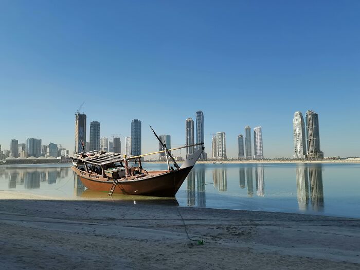 Traditional wooden boat on calm water with a modern city skyline in the background for a cities quiz challenge