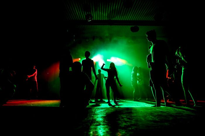 Silhouettes of people in a dark room with green and red lighting, capturing bizarre moments that feel surreal and strange.
