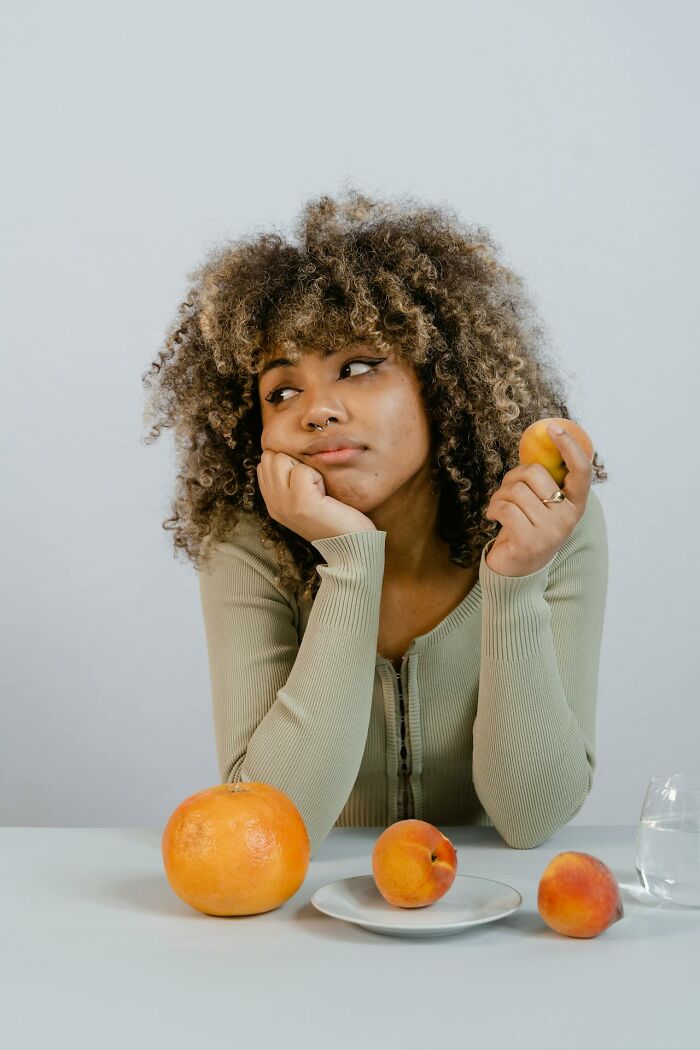 Young woman with curly hair holding fruit, looking away thoughtfully, a visual contrasting calm with Karen behavior examples.