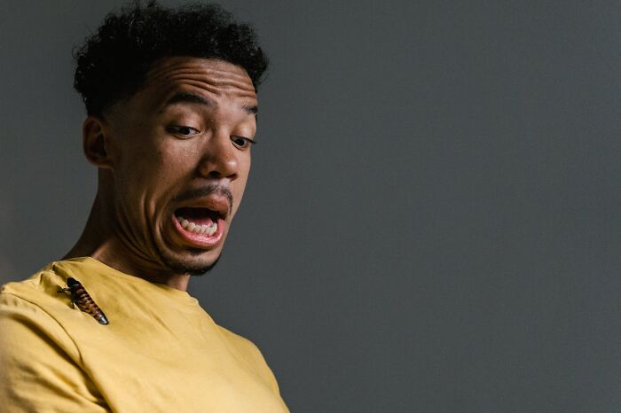 Man in yellow shirt reacting with horror to a large insect on his shoulder, illustrating garbage men finding something horrifying on the job