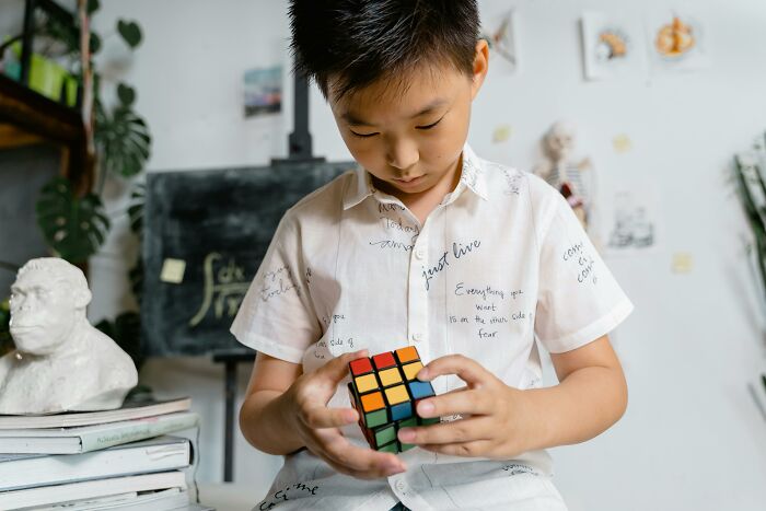 Young boy focused on solving a Rubik's cube puzzle, engaging in mind-bending visual challenges at home.