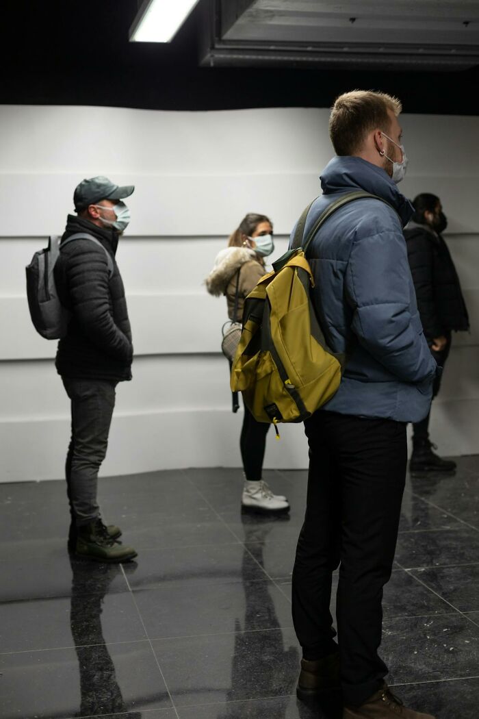 People wearing masks and backpacks standing spaced apart indoors, illustrating examples of Karens behavior.
