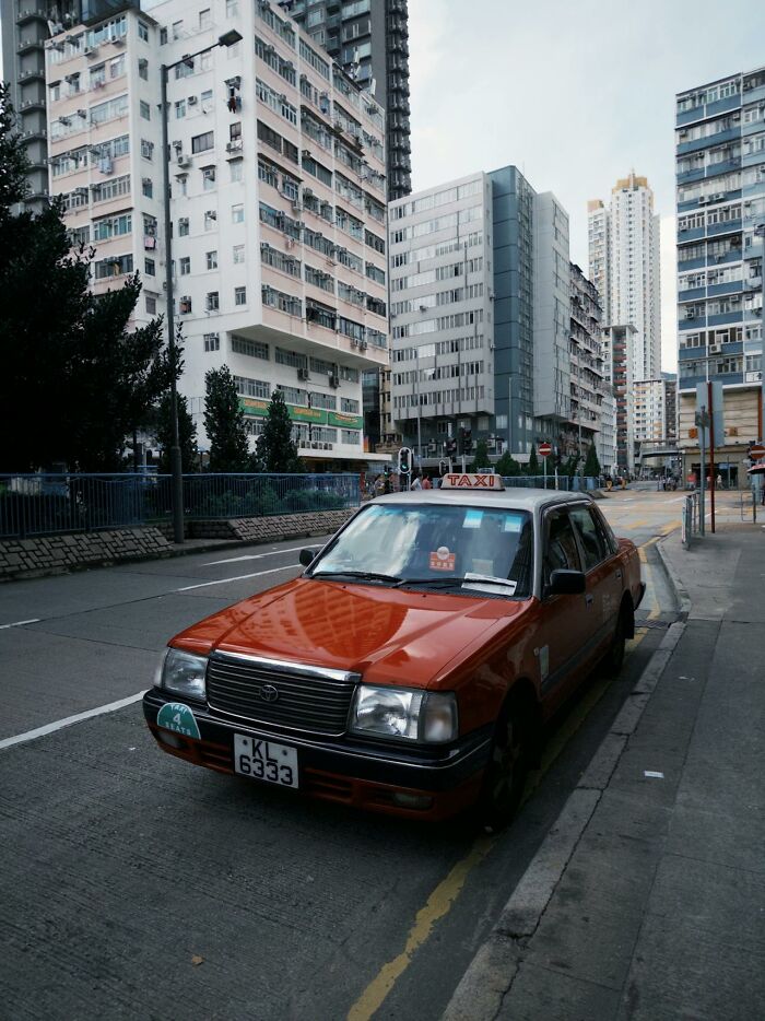 Red taxi parked near high-rise buildings in city street, urban scene captured with Karen examples keyword focus.