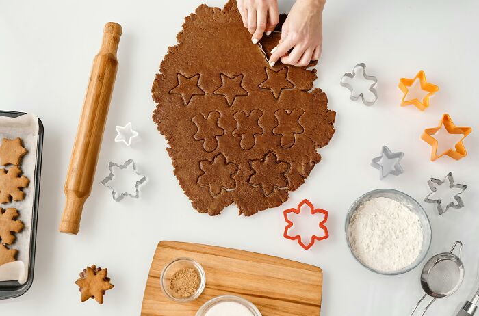 Hands cutting star-shaped cookies from brown dough with cookie cutters and baking tools, illustrating petty revenge theme.