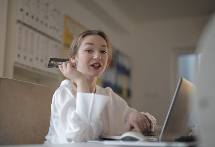 Young woman holding credit card near laptop, illustrating examples of Karens so crazy in an office setting.
