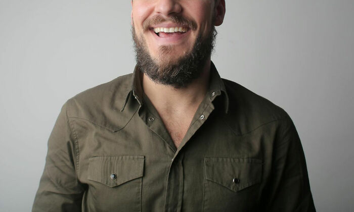 Bearded man in casual olive shirt smiling, illustrating emotional intensity shared by nurses in psych wards.