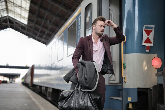 Man in a maroon suit carrying bags and looking stressed while standing next to a train at a station, Karen examples concept.