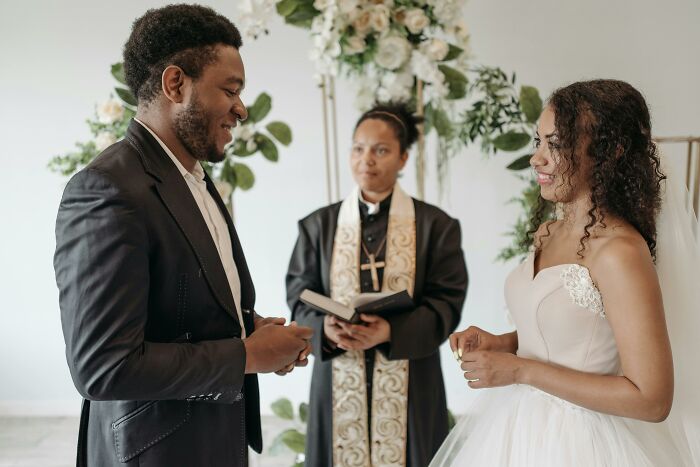 A couple exchanging rings during a wedding ceremony, highlighting life moments that seem compulsory but are optional.