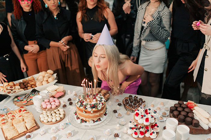 Woman in a party hat blowing out candles on a cake while guests watch, highlighting rich man refuses to pay dispute.