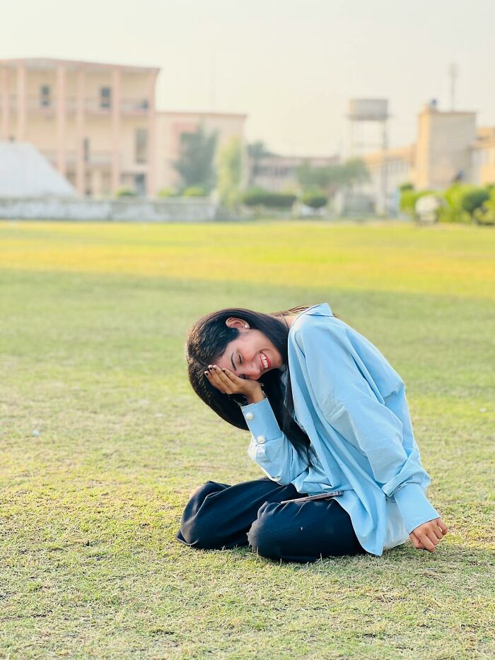 Young woman sitting on grass outdoors, smiling and covering face, illustrating examples of Karens so crazy it's kinda scary.