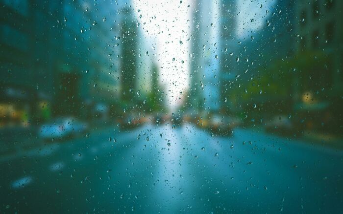 Raindrops on window with blurred city street background, challenging viewers to identify objects and test visual IQ.