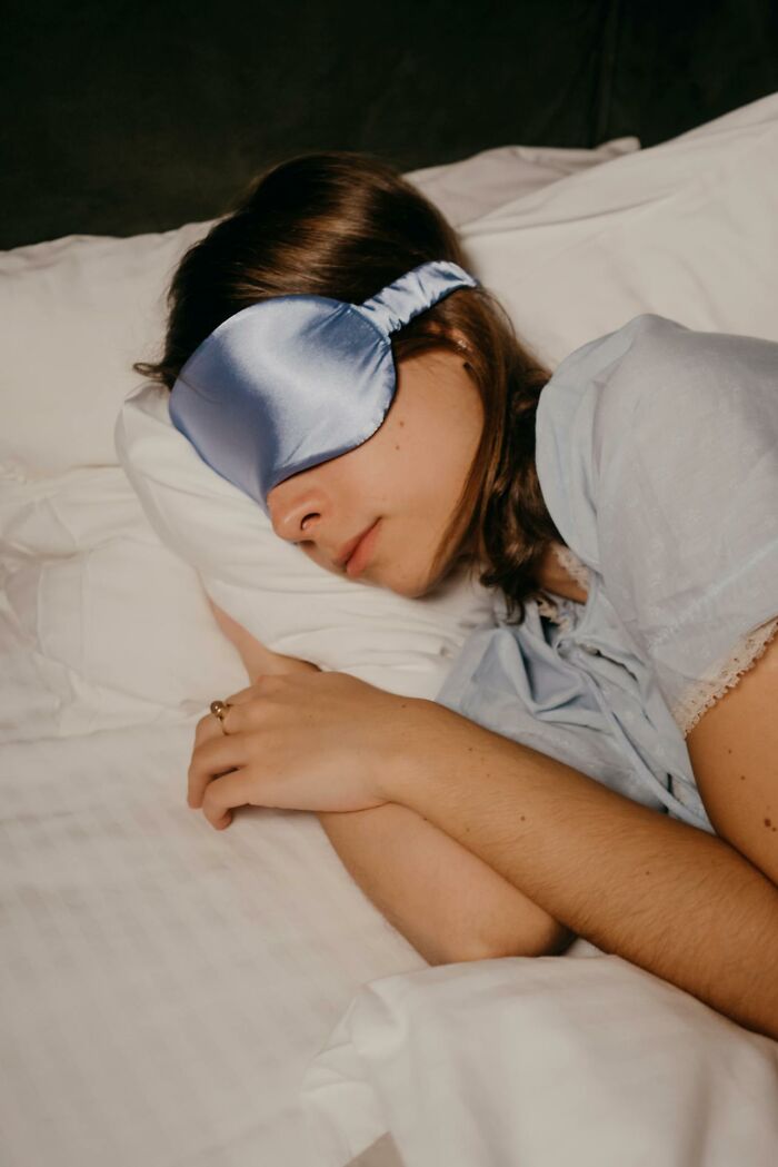 Young woman wearing a blue sleep mask lying in bed, illustrating experiences of people who came back to life.
