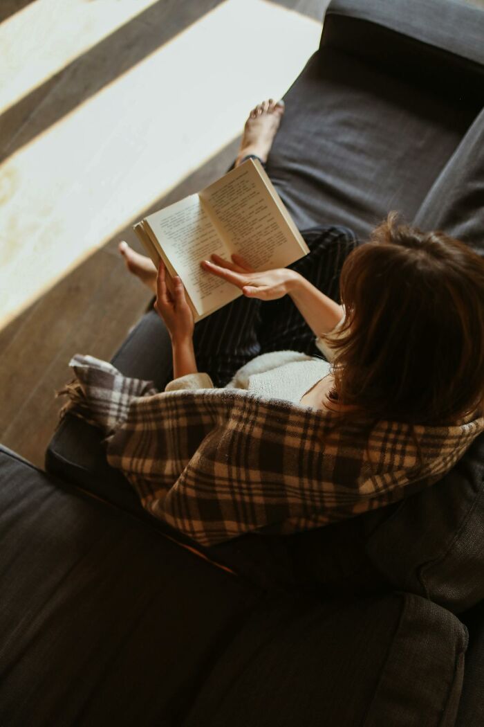 Person wrapped in plaid blanket reading a book on a couch, reflecting on unusual childhood habits and experiences.