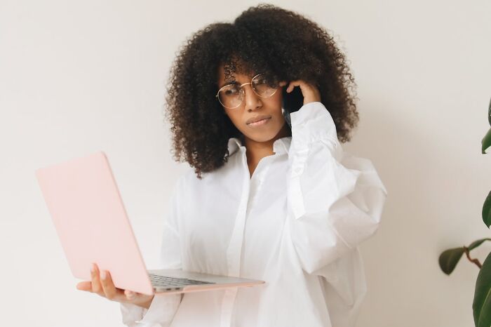 Young woman with curly hair and glasses holding a laptop, appearing thoughtful in a minimalistic setting related to Karens examples.