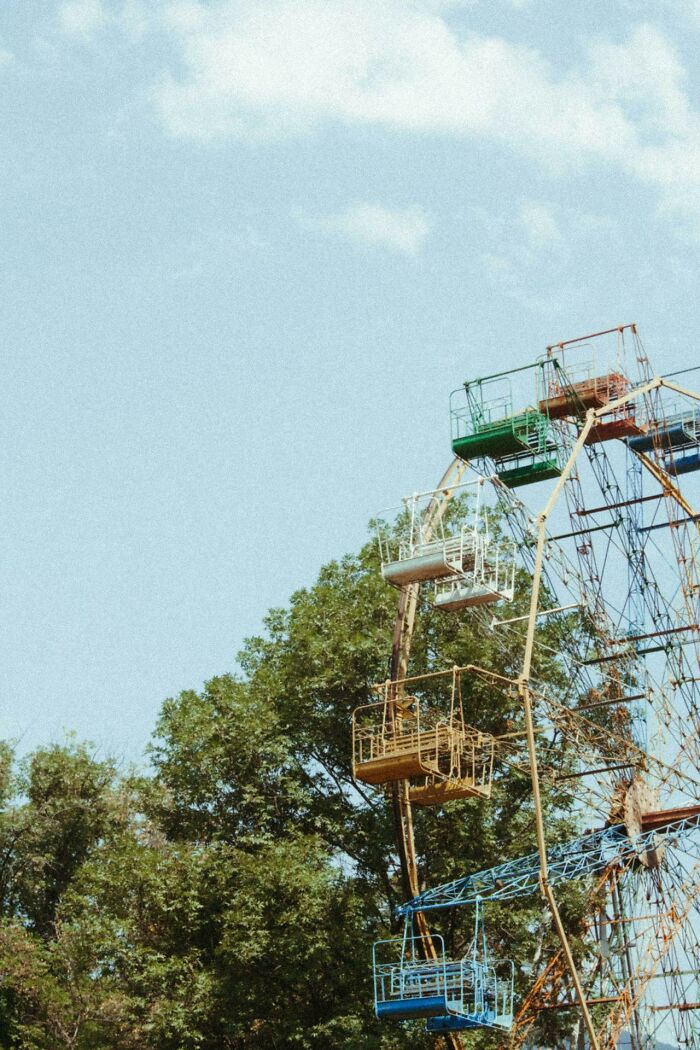 Rusty Ferris wheel with faded colorful seats surrounded by trees, evoking bizarre and creepy park ranger sightings.
