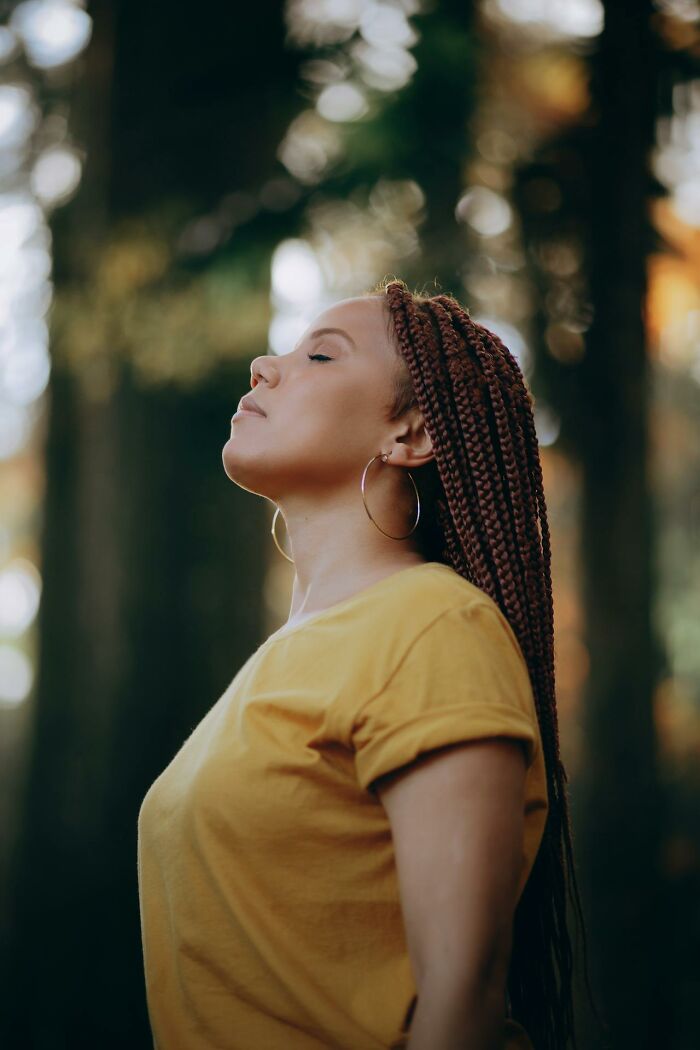Woman with braided hair and hoop earrings standing outdoors with eyes closed, reflecting on dying and coming back to life experience