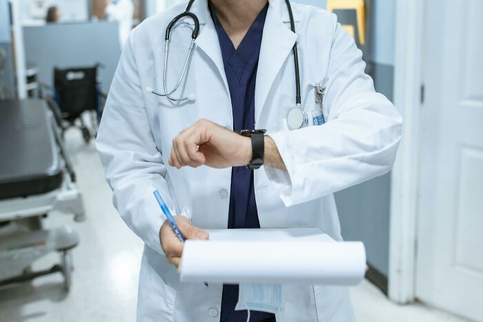 Doctor in white coat with stethoscope writing notes while checking time in hospital hallway during real-life horror story situation