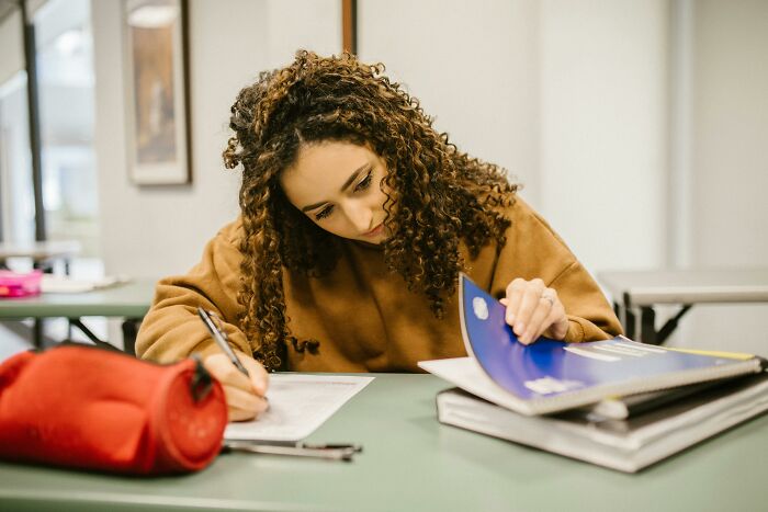 Student with curly hair focused on test papers and notebooks, practicing to test IQ against the average U.S. student. Student with curly hair focused on test papers and notebooks, practicing to test IQ against the average U.S. student.