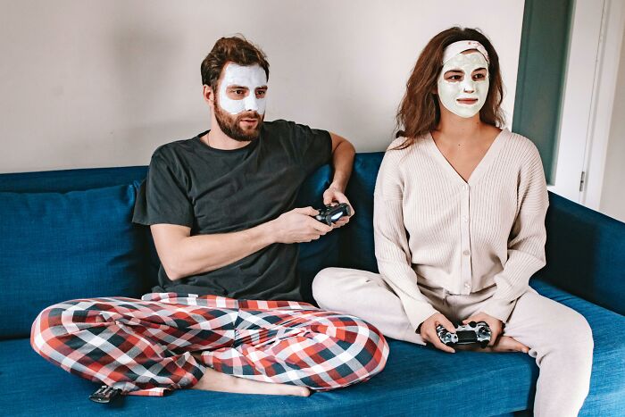 Couple with facial masks playing video games on a couch, illustrating relatable and ridiculous everyday moments.