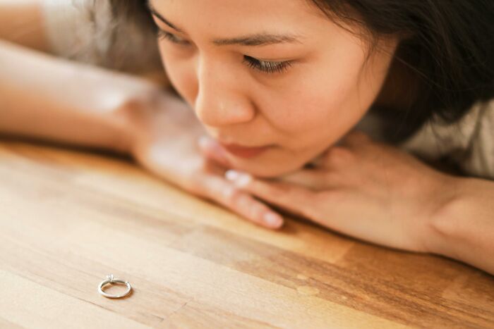 Young woman looking sadly at a ring on a wooden table, reflecting on toxic relationship traits and emotional pain.
